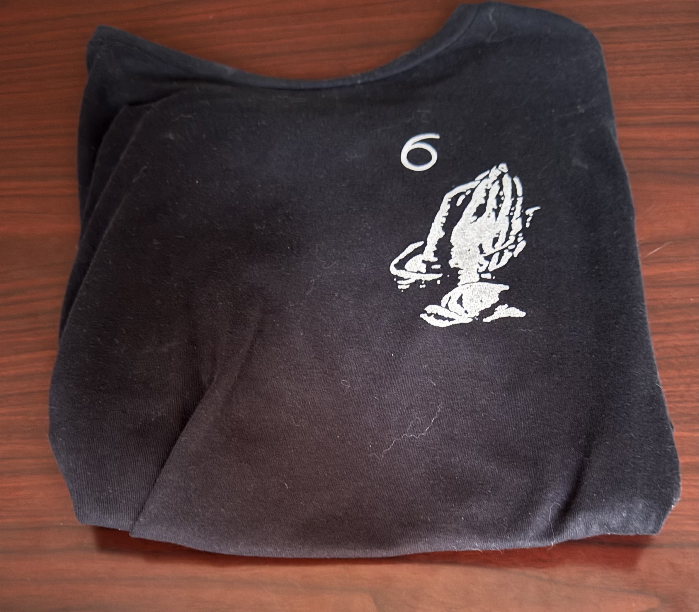 The shirt depicts a logo from the rapper “Drake” with two hands in supplication.
